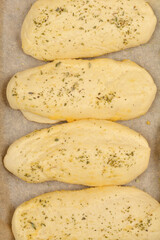 A close-up shows several golden-brown bread rolls seasoned with garlic and oregano, suggesting a...