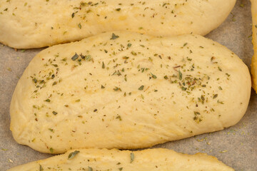A close-up shows several golden-brown bread rolls seasoned with garlic and oregano, suggesting a flavorful and aromatic baked good