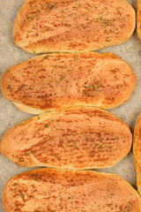 Several golden-brown garlic and oregano rolls are arranged on a baking pan lined with parchment paper
