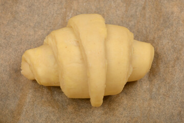 A single, unbaked croissant dough rests on a piece of parchment paper, ready for the oven