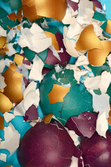 A close-up top-down view shows shattered and peeled colorful Easter eggshells in shades of gold,...