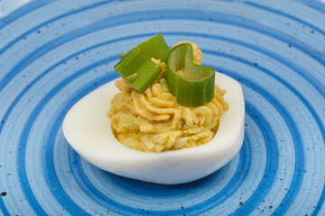A close-up top-down view shows a deviled egg, filled with a creamy avocado and yolk mixture and garnished with green onions, on a blue and white swirled plate