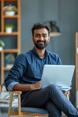 Young thoughtful bearded smart indian professional business man executive looking away sitting on chair in modern office lobby using laptop, thinking of new ideas, planning project, working online.