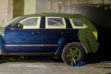 A blue SUV stands in a dimly lit industrial garage. Its windows are covered with plastic, and the...