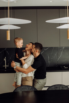 Happy family embracing in modern kitchen: father lifting son, mother smiling