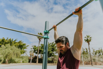 A man is holding a high bar at a calisthenics gym during a workout ready to do pull ups