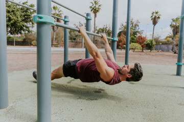 A man is doing Australian pull ups doing his workout outside, horizontal photo