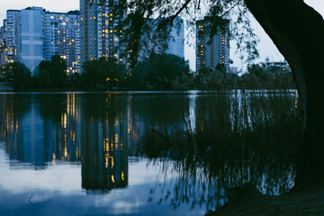 A tranquil evening scene of a lake reflecting city lights, buildings and water creating a mirrored...