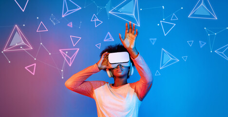 African girl with VR glasses standing at blue and pink background and looking at floating geometric shape. Excited person searching and entering visual reality world. Technology innovation. Ingenuity.