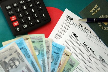 Bangladeshi taka money bills lies on table with pen, calculator, passport and tax forms