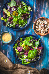Fresh salad with mixed varieties and edible flowers on a blue wooden background