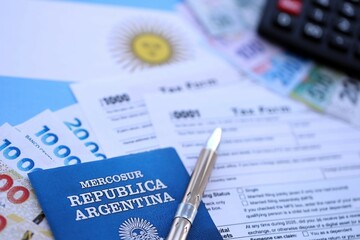 Argentine pesos money bills in big amount lies on table with pen, calculator, passport and tax forms