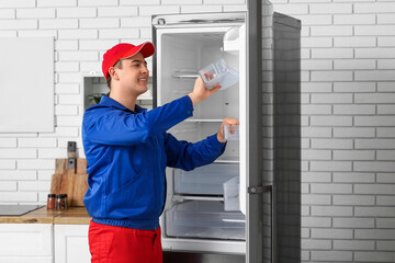 Happy male worker repairing refrigerator in kitchen