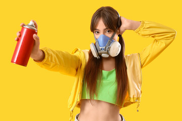 Young girl in respirator and with spray can on yellow background