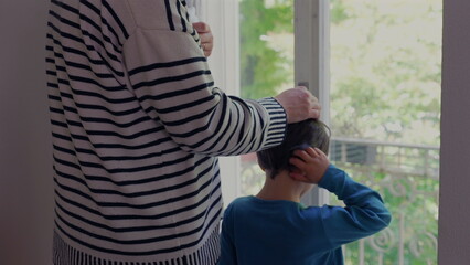 Mother standing with her young son by the window, hand gently placed on his head, conveying a tender moment of support and care. the deep bond between mother and children-SD 480p