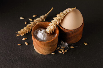 Wheat, flour and egg. Group of food products - egg, wheat ears and flour in a wooden bowl on a black background.