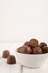 Chocolate candies with nut filling in a white bowl on a light wooden surface. One candy is broken, two are placed nearby. Clean and minimalist composition.