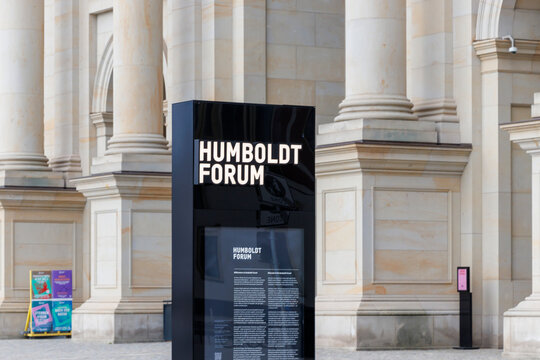 Berlin, Germany - April 11, 2025: A modern information stand displaying details about Humboldt Forum, standing near classical architectural pillars in the heart of the city.