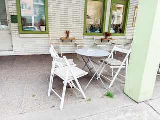 Simple cafe patio with folding white chairs and round metal table against brick wall. Casual street dining and social outdoor space
