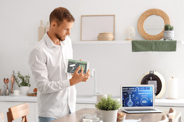 Young man using smart home security system control panel in kitchen