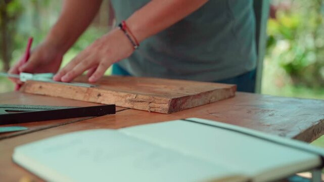Young man marking rough wood with ruler and pencil to square it on rustic outdoor table
