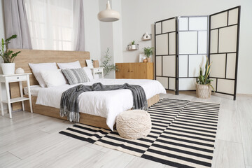 Interior of light bedroom with cozy bed and stylish folding screen
