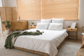 Comfortable bed with plaid and chest of drawers in interior of bedroom