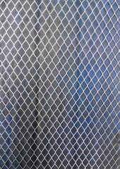 Metal mesh with diamond-shaped cells. Iron sheets partially covered with blue paint in the background
