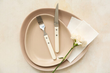 Plates with cutlery, paper napkins and carnation on beige grunge background