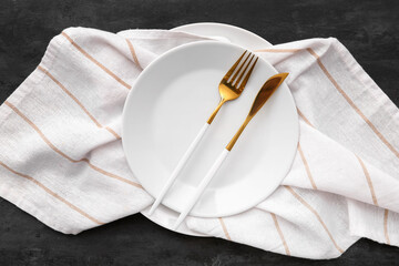 Plate with cutlery and napkin on black grunge background