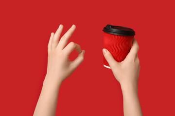 Female hands with takeaway cup of coffee showing OK on red background