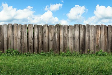 Rustic wooden fence with barbed wire and open field under blue sky