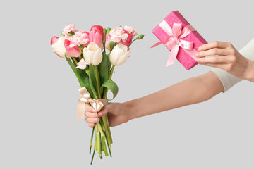 Young woman holding gift box and bouquet of beautiful flowers for Mother's Day on grey background, closeup