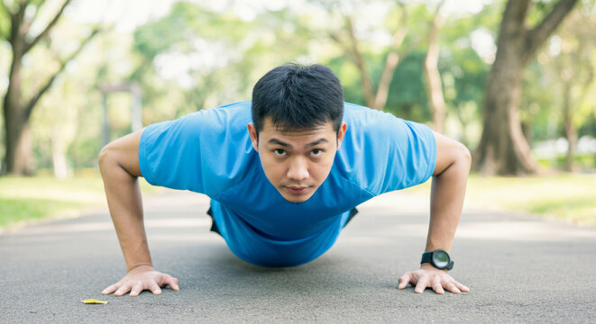Asian young male doing push-ups on outdoor path in park setting