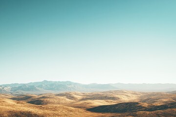 Naklejka premium Vast, arid landscape under a clear, pale blue sky. Rolling hills extend to distant mountains.