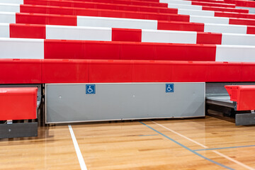 Accessible symbol on the front row of red and white plastic interior gymnasium bleachers.

