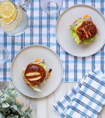 Table top picnic lunch with plaid tablecloth and sandwiches on plates with a pitcher of water with lemons