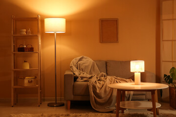 Interior of night living room with sofa, shelving unit, glowing lamps and coffee table