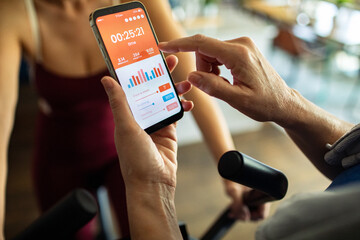 Senior lesbian couple tracking workout stats on fitness app during exercise bike session