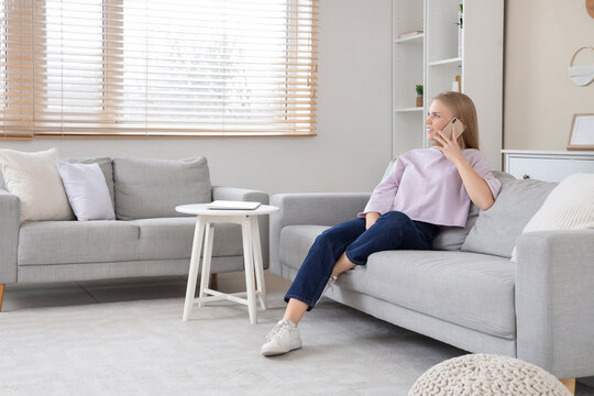 Young blonde woman talking by mobile phone on sofa at home