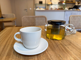Glass teapot with herbal infusion and white ceramic cup on cafe table. Relaxation and modern tea culture