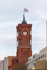 Obraz premium Historical red clock tower in Berlin, Germany, showcasing its intricate architecture and a flag waving atop. Ideal for themes of history and city landmarks.