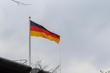 German flag waving on a pole against a cloudy sky, symbolizing national pride and unity. The flag...