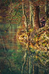 A teenage girl stands on a vibrant autumn forest trail, holding a camera and taking pictures of the breathtaking natural beauty around her.