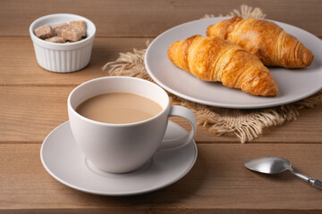 Freshly baked croissants served with a hot cup of coffee on a wooden table in a cozy setting
