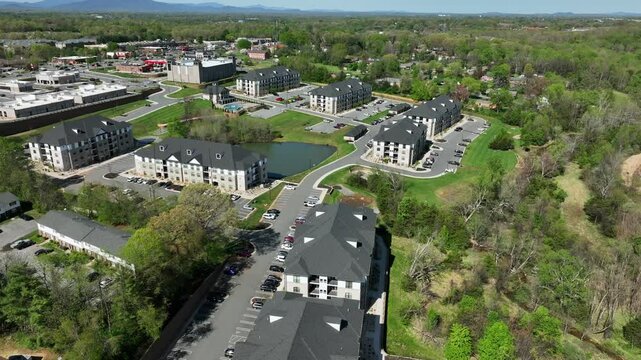 Modern apartment buildings with private lake in center. American suburb town with luxury multi-family units in spring season. Aerial approaching top down.