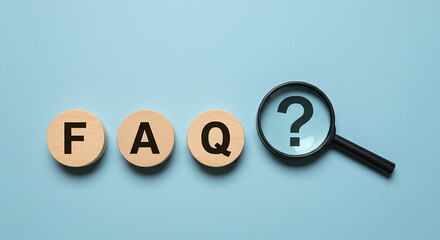 Frequently Asked Questions concept with FAQ letters on circular wooden blocks and a magnifying glass over a question mark on a blue background, representing customer support and information search