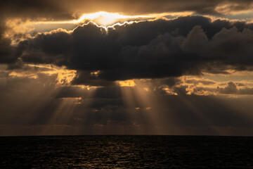 Dazzling sunlight breaks through clouds over ocean at sunset