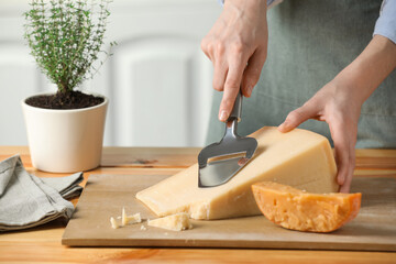 Woman cutting delicious cheese with slicer at wooden table indoors, closeup