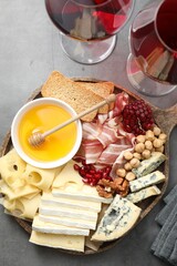 Different types of cut cheese and other snacks served with wine on gray textured table, flat lay